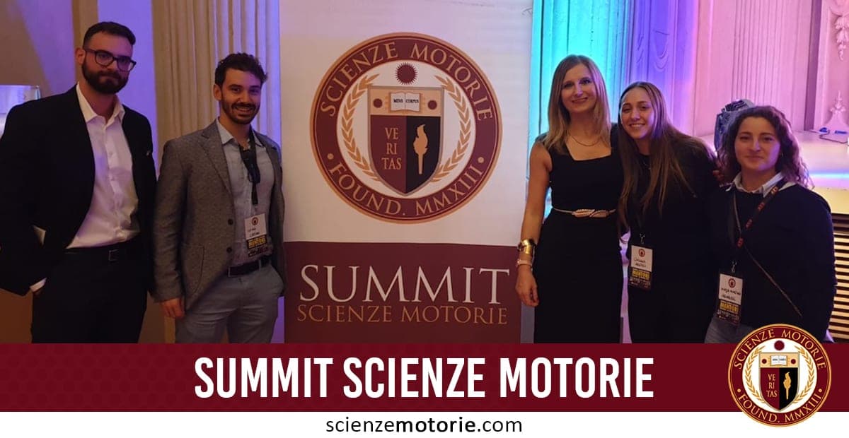 Cinque persone in abbigliamento formale posano accanto a un cartellone con il logo e titolo "Summit Scienze Motorie" durante un evento interno ben illuminato.
