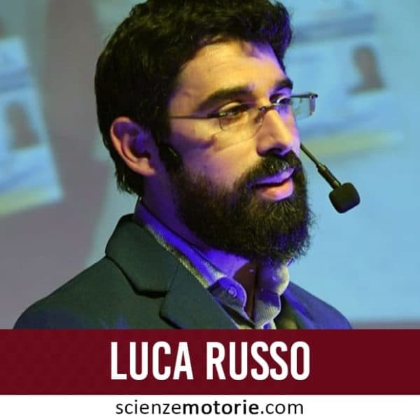 Luca Russo durante una presentazione con microfono ad archetto in una sala conferenze, sfondo con proiezione sfocata, logo scienzemotorie.com in basso a destra.