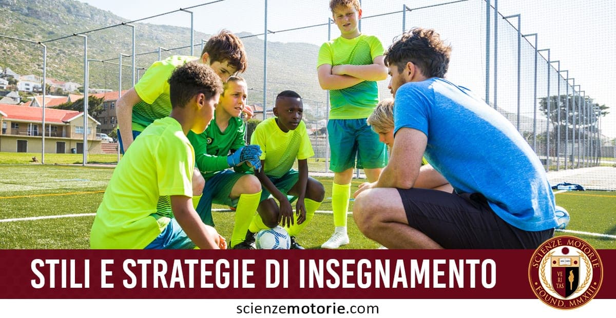 L’immagine mostra un gruppo di ragazzi in tenuta sportiva in cerchio attorno a un allenatore accovacciato, su un campo da calcio all’aperto con montagne sullo sfondo. La scena evidenzia l’importanza della comunicazione e dell’uso di strategie didattiche nello sport giovanile. Il logo Scienze Motorie e la scritta “Stili e Strategie di Insegnamento” collegano l’immagine a contenuti formativi per allenatori ed educatori motori.