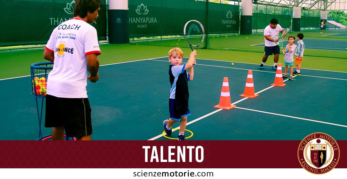 L'immagine mostra un campo da tennis con alcuni bambini che stanno partecipando a una lezione di tennis. In primo piano, c'è un bambino che sta colpendo una palla con la racchetta, mentre un allenatore lo osserva. Sullo sfondo, ci sono altri bambini che aspettano il loro turno vicino a dei coni arancioni e un altro istruttore. Sulla parte inferiore dell'immagine, c'è un banner con la scritta "TALENTO" e un logo con il testo "SCIENZE MOTORIE".