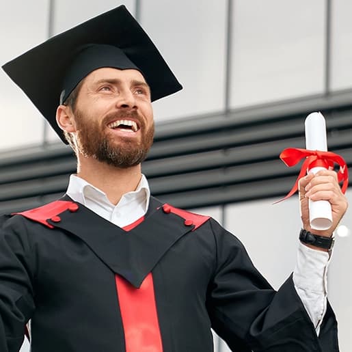 Uomo sorridente in toga e cappello da laurea con diploma in mano davanti a un edificio universitario moderno, logo scienzemotorie.com visibile.